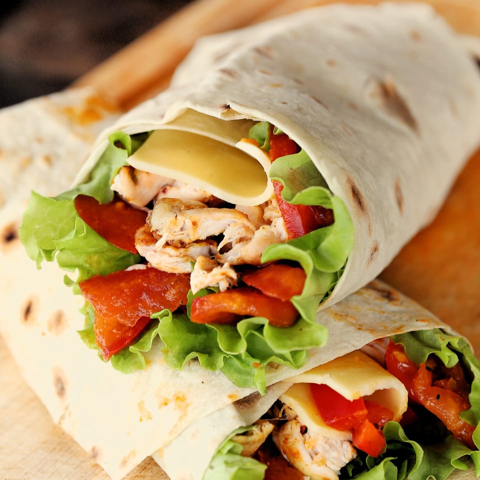 Two chicken wraps with lettuce, cheese, and red peppers on a wooden surface.