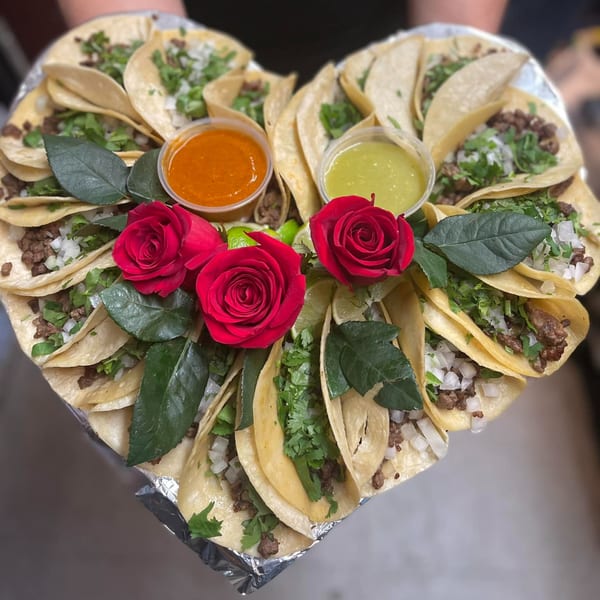 Heart-shaped platter of El Vaquero Mexican Restaurant tacos with red roses and two dipping sauces.