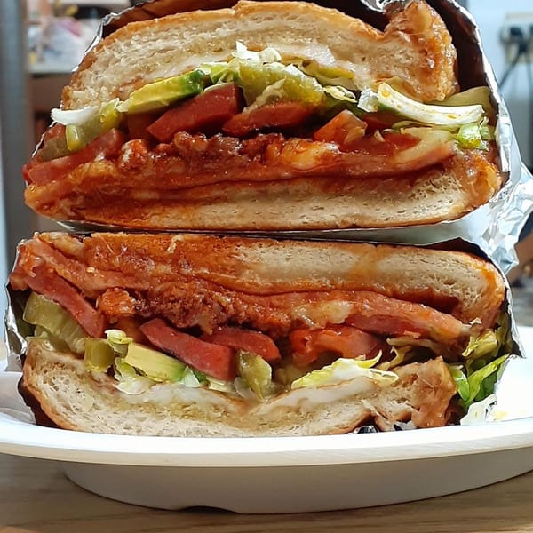 A large Mexican torta sandwich, cut in half, revealing layers of meat, lettuce, avocado, and sauce.