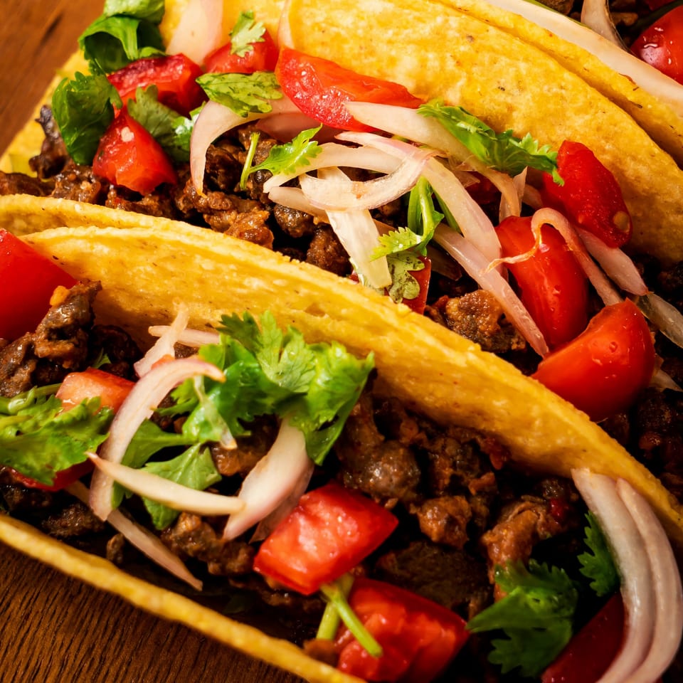 Close-up of three El Vaquero Mexican Restaurant tacos filled with meat, tomatoes, onions, and cilantro.