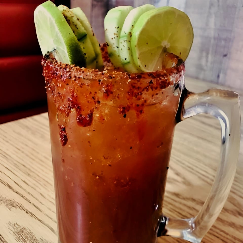 A large El Vaquero Michelada with a chili-salted rim, garnished with lime and cucumber slices.